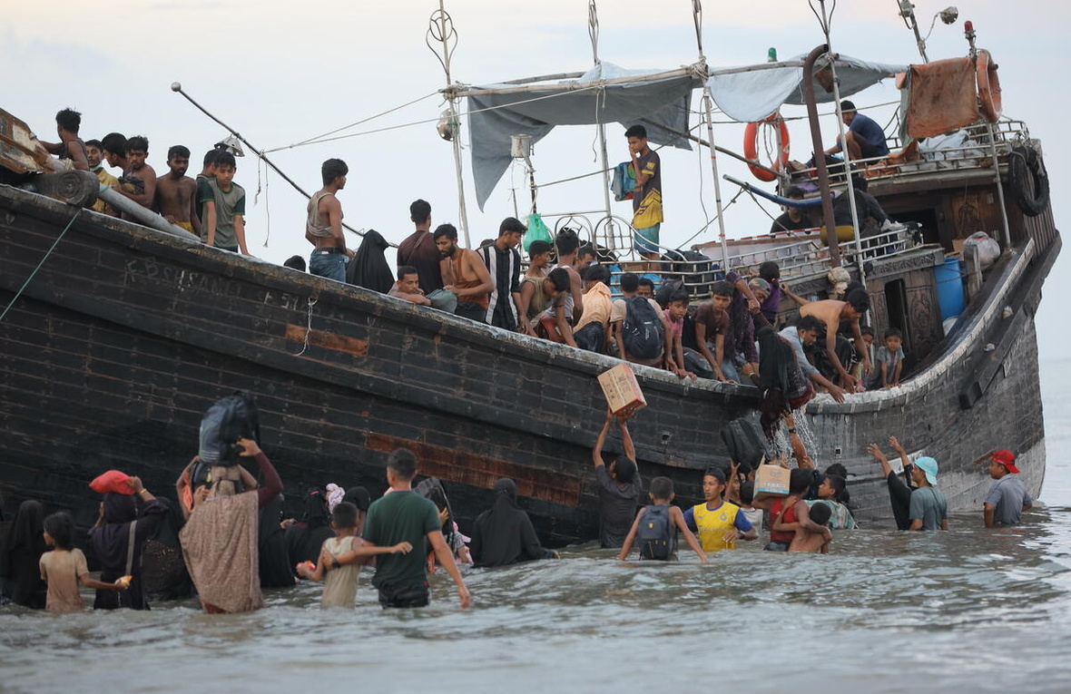Rohingya refugees disembarking from a crowded vessel in shallow water in North Aceh, Indonesia