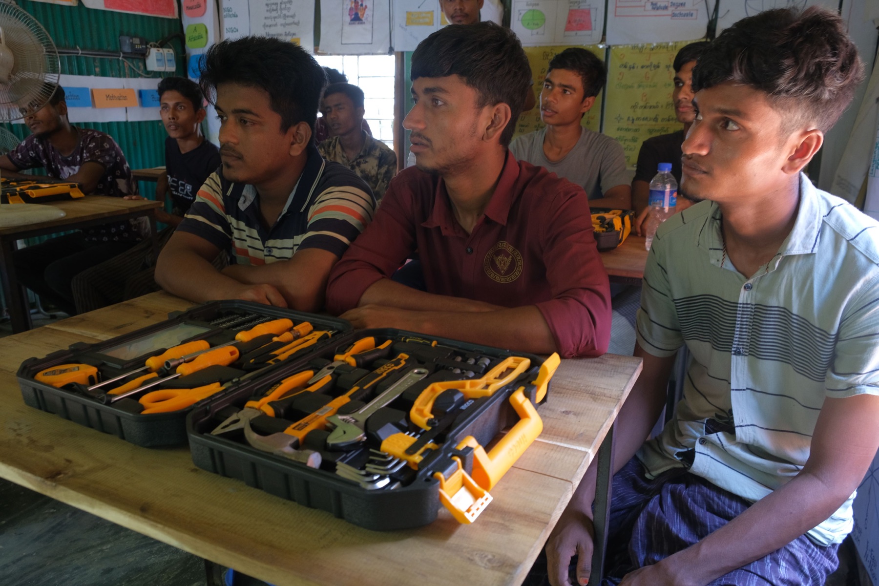 Young Rohingya men taking part in a vocational training session with toolkits on the desks